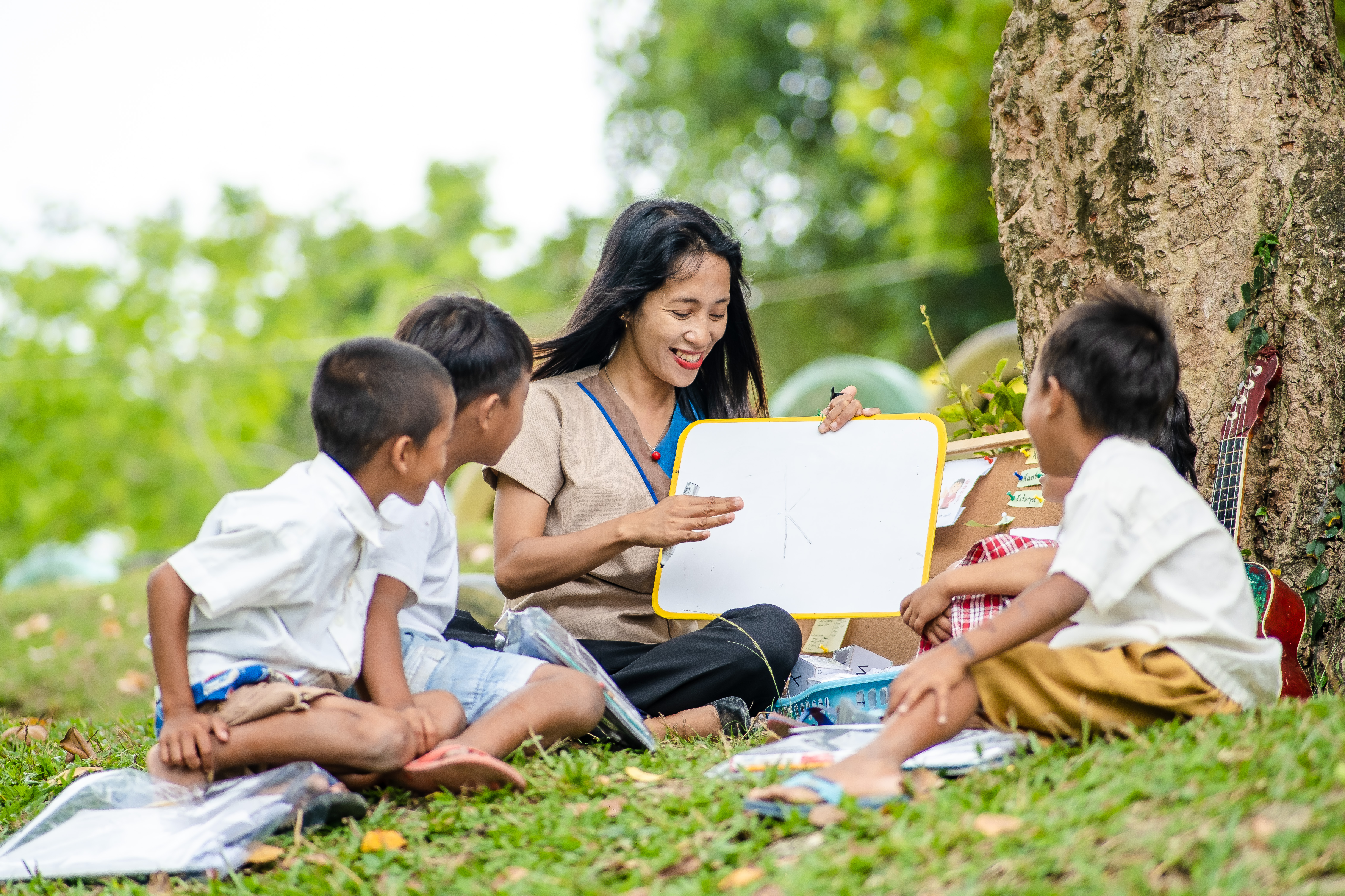 A Teacher Fellow reading to three students outdoors.